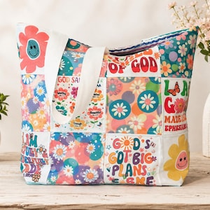 May include: A patchwork tote bag with a variety of floral and inspirational designs. The bag features a white strap and is decorated with colorful flowers, butterflies, and phrases like "God's Got Big Plans".