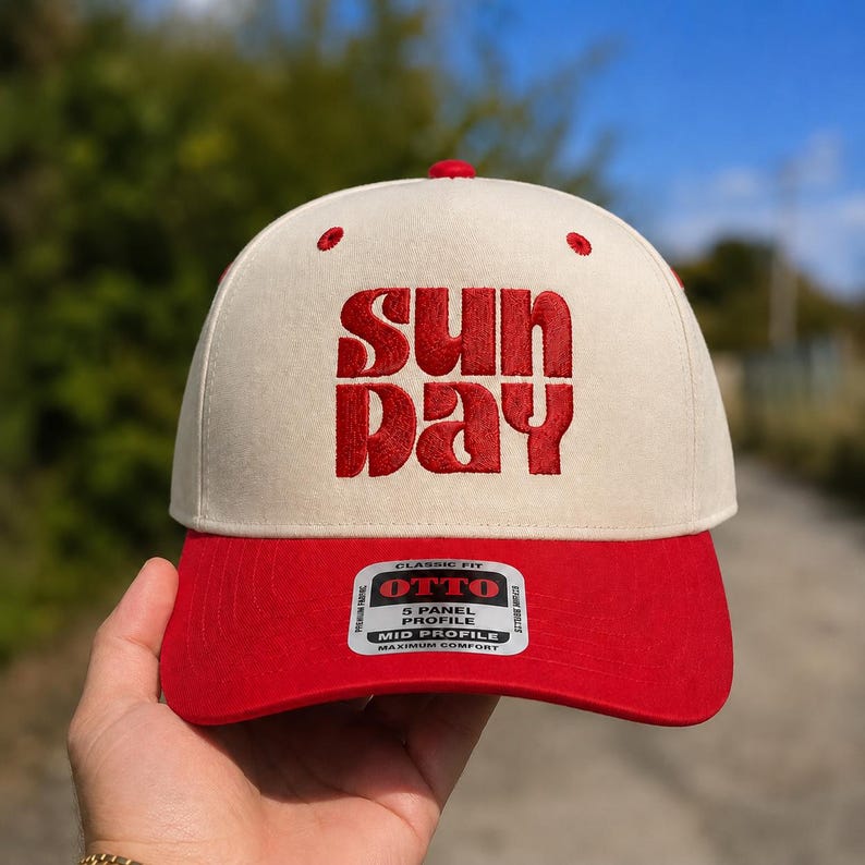 Pode incluir: Um bon&eacute; de beisebol de cinco pain&eacute;is com coroa na cor creme e aba vermelha. A parte frontal apresenta a palavra "SUN DAY" bordada em letras vermelhas em negrito. Um adesivo retangular na aba diz "OTTO 5 PANEL PROFILE MID PROFILE".