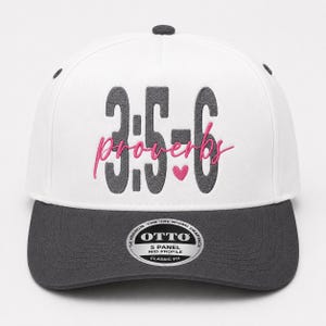 Può includere: Un cappellino snapback bianco a cinque pannelli con visiera e bottone superiore grigio scuro. La parte anteriore presenta il testo ricamato grigio scuro 3:5-6 con la parola proverbs in corsivo rosa e un piccolo cuore rosa. Un adesivo Otto è sulla visiera.