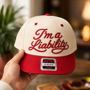 Può includere: Un cappellino snapback color crema con il testo ricamato in rosso I'm a Liability sulla parte anteriore. Il cappellino presenta una visiera rossa tinta unita e un bottone rosso sulla sommità. Un adesivo rettangolare sulla visiera riporta OTTO S-N-A-P.