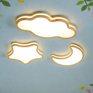 May include: A set of three wooden ceiling lights shaped like a cloud, star, and crescent moon. The lights have a warm, natural wood finish and emit a soft, white glow. The lights are mounted on a light blue ceiling with decorative elements.