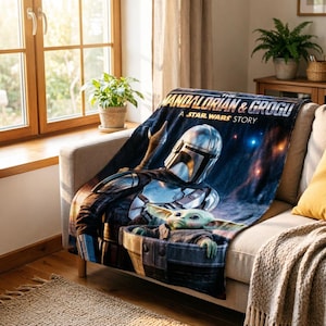 May include: A navy blue blanket featuring the Mandalorian and Grogu from "The Mandalorian: A Star Wars Story." The blanket displays the characters in a space scene with the text "The Mandalorian & Grogu" in white.