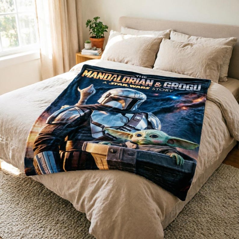 May include: A navy blue blanket featuring the Mandalorian and Grogu from The Mandalorian. The blanket displays the characters in a dynamic pose against a space-themed backdrop, with the text "THE MANDALORIAN & GROGU A STAR WARS STORY".