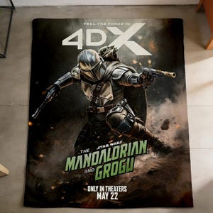 May include: A blanket featuring a dynamic illustration of The Mandalorian and Grogu from Star Wars. The artwork depicts the characters in action, with the text "FEEL THE FORCE IN 4DX" and "ONLY IN THEATERS MAY 22". The blanket is on a gray surface.