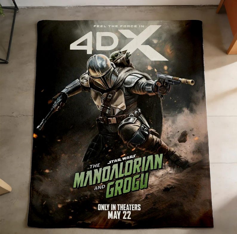 May include: A blanket featuring a dynamic illustration of The Mandalorian and Grogu from Star Wars. The artwork depicts the characters in action, with the text "FEEL THE FORCE IN 4DX" and "ONLY IN THEATERS MAY 22". The blanket is on a gray surface.