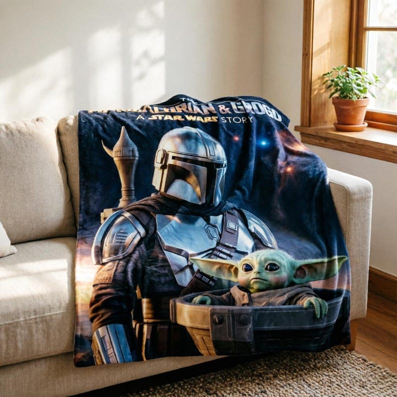May include: A navy blue throw blanket featuring The Mandalorian and Grogu from the Star Wars series. The blanket displays the characters in a detailed graphic, with the text "THE MANDALORIAN & GROGU A STAR WARS STORY". The blanket is draped over a beige sofa.