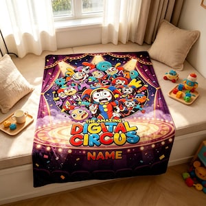 Puede incluir: Una manta rectangular de forro polar con un estampado gráfico colorido de los personajes de The Amazing Digital Circus. El diseño incluye una escena circular central con varias figuras de dibujos animados, el título del programa y un espacio para un nombre.