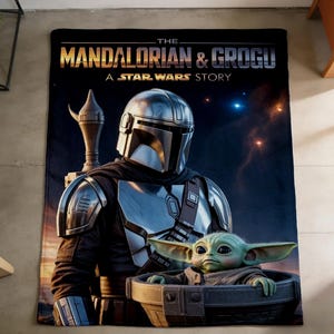 May include: A black blanket featuring the Mandalorian and Grogu from the Star Wars series. The Mandalorian is in silver armour, and Grogu is in a dark grey carrier. The blanket has the text "THE MANDALORIAN & GROGU A STAR WARS STORY".