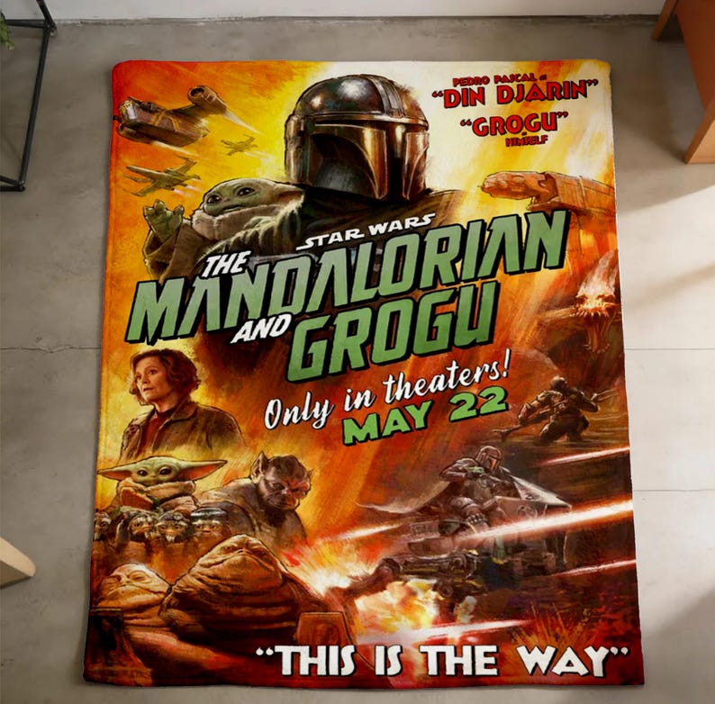 May include: A Star Wars themed blanket with a movie poster design for "The Mandalorian and Grogu". The image features the Mandalorian, Grogu, and other characters. The text reads "Only in theaters! MAY 22" and "THIS IS THE WAY."