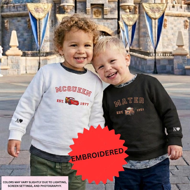 Two young children, a boy and a girl, are standing together and smiling in front of a castle. They are wearing sweatshirts with the text "McQueen" and "Mater" printed on them.