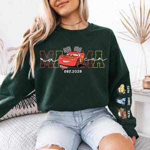 A woman wearing a green sweatshirt with a graphic of a red car and the text "MOMA" printed on it.