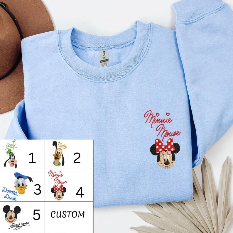 A light blue t-shirt with a Minnie Mouse embroidered on the front, along with a hat and some leaves.