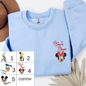 A light blue t-shirt with a Minnie Mouse design and a list of numbers below it, along with a brown hat and some leaves.