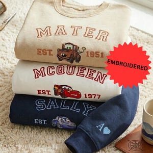 a stack of three sweatshirts with various Disney character designs, including a character from the Cars movie franchise.