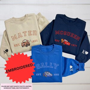 a collection of four sweatshirts, each featuring a different character from the Cars movie franchise. The sweatshirts are arranged on a white background, with a red starburst graphic in the foreground.