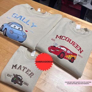 three t-shirts with different car designs and text, including a blue car and two red cars, along with the text "SALLY" and "McQueen" printed on them.