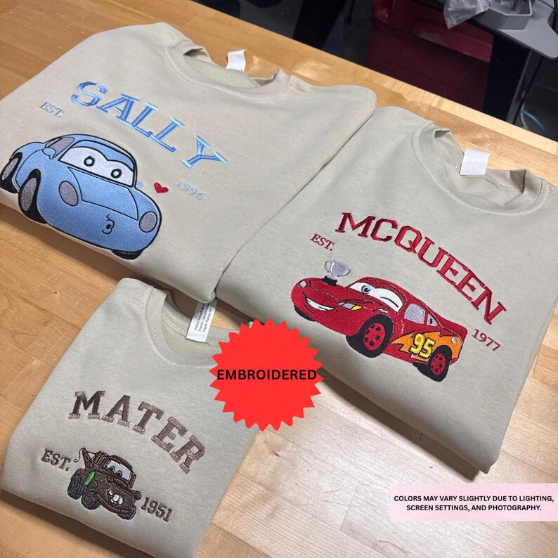 three t-shirts with different car designs and text, including a blue car and two red cars, along with the text "SALLY" and "McQueen" printed on them.