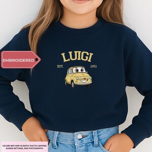 A person wearing a navy blue sweatshirt with a yellow cartoon car and the text "LUIIGI EST. 1951" printed on it.