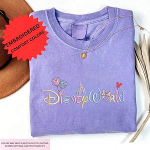 a purple t-shirt with the Disney World logo embroidered on it, along with a necklace and a hat.