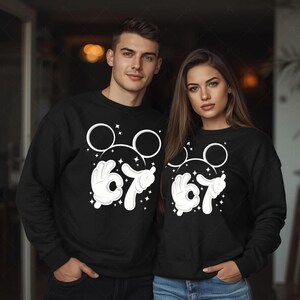 A man and a woman are standing together, both wearing black sweatshirts with white Mickey Mouse designs.