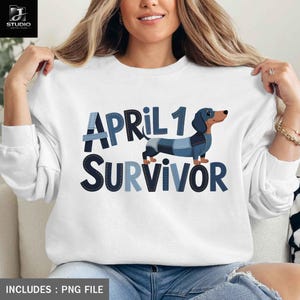 Puede incluir: Sudadera blanca con el texto "APRIL 1 SURVIVOR" en letras azules estilo denim. Un perro salchicha de dibujos animados con un diseño de patchwork azul aparece entre las palabras. La sudadera es un archivo PNG.