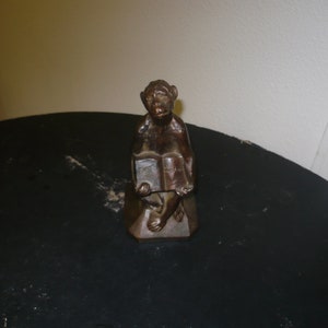 May include: A bronze figurine of a monkey sitting on a base, holding a book in its hands.