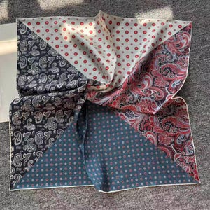 May include: A silk scarf with a patchwork design. The scarf features four distinct patterns: white with red polka dots, navy with paisley, teal with red polka dots, and red paisley. The scarf is folded and knotted.
