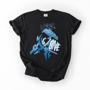 May include: Black t-shirt with a blue graphic design. The design features the text "G Zone" with a stylized raven and other abstract shapes. The shirt is made of a soft material and has a classic crew neck.