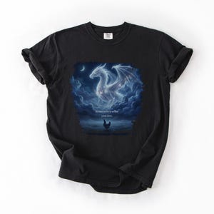 May include: Black t-shirt featuring a fantasy art design. The graphic depicts a white dragon with outstretched wings, surrounded by clouds and a crescent moon. The text "Remember who you are" is below the dragon, with a chicken silhouette.
