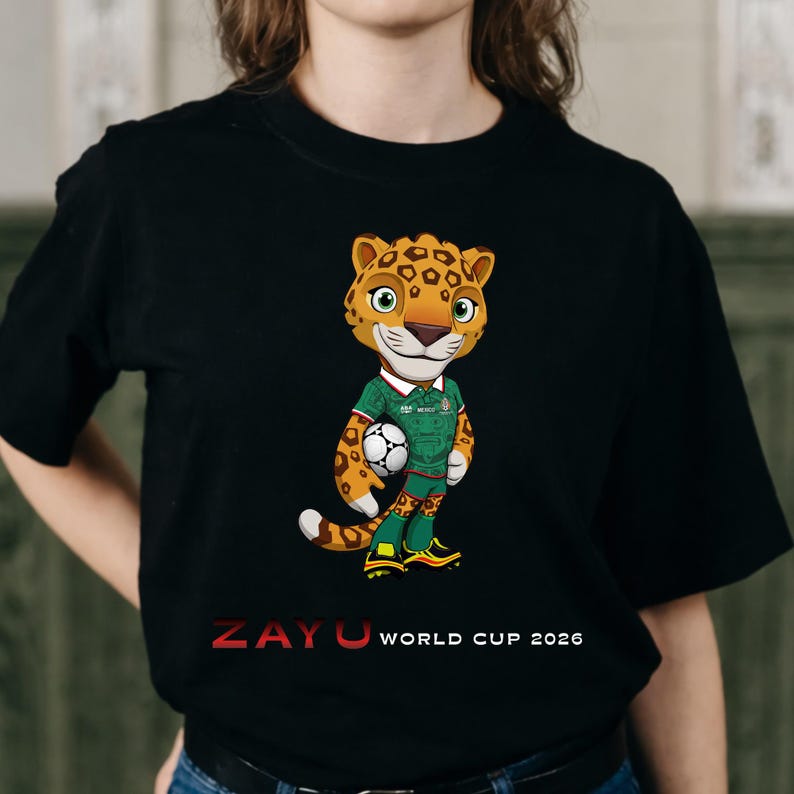 May include: Black t-shirt featuring a cartoon jaguar mascot holding a soccer ball. The jaguar wears a green and white soccer uniform. The text "ZAYU WORLD CUP 2026" is printed in red and white below the jaguar.