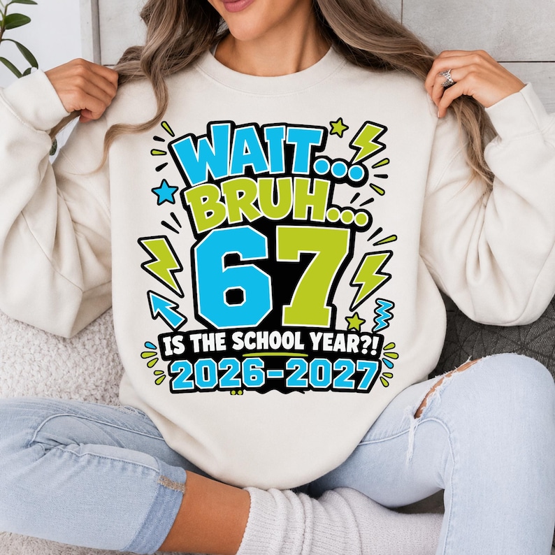 May include: A cream-colored crewneck sweatshirt featuring a graphic print in blue, lime green, and black. The text reads: WAIT... BRUH... 67 IS THE SCHOOL YEAR?! 2026-2027. The design includes lightning bolt and star accents surrounding the large numbers.