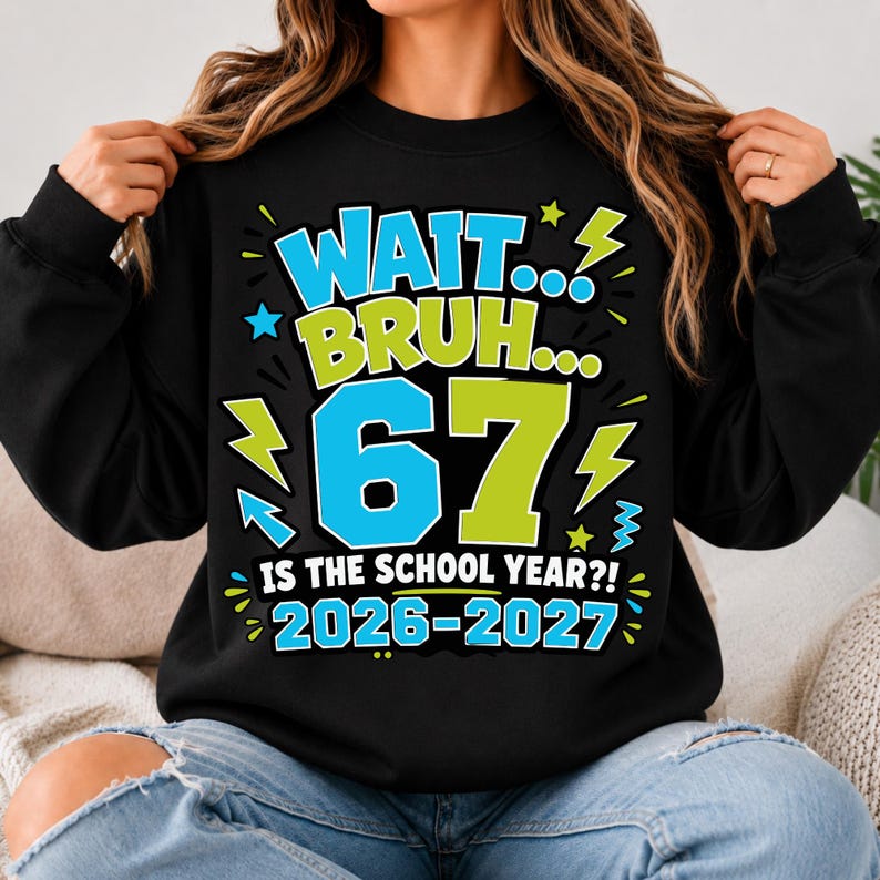 May include: A black long-sleeve sweatshirt featuring a graphic print with the text "WAIT... BRUH... 67 IS THE SCHOOL YEAR?! 2026-2027". The design includes large blue and lime green numbers and letters, accented by small lightning bolt and star shapes.