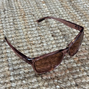 Peut inclure: Lunettes de soleil mauves avec une monture rectangulaire et des verres teintés marron. Les lunettes sont fabriquées dans un matériau translucide et ont un design épuré. Les branches sont légèrement incurvées pour un ajustement confortable.