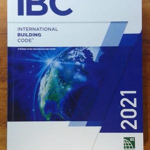 May include: A book titled "IBC International Building Code 2021." The cover features the letters "IBC" in large, white font at the top, with the title below. A blue and white graphic of Earth is on the cover.