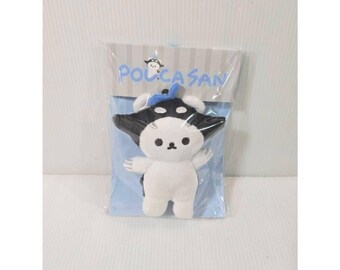 May include: A small plush toy featuring a white body and a black hood with a blue bow, packaged in a clear plastic bag. The packaging displays the text "POCHACCO" in blue letters above the plush, along with a small graphic of a cartoon character.