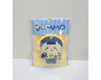 May include: A small plush doll featuring a character with dark hair, red spiral cheeks, and a blue outfit with a yellow sun-shaped collar. The doll is packaged in a clear plastic bag with a blue and yellow cardboard header labeled GÜMMO.