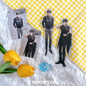 May include: An assortment of anime character merchandise, including acrylic standees and character cards. The standees depict a man in a black outfit and gray pants. The character cards feature the names "KIM DOKJA" and "YOO JOONG HYUK". The background is a yellow and white checkered pattern.