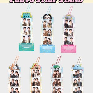 May include: Seven GMMTV Character Photo Strip Stands featuring vertical acrylic frames with colourful bases, patterned borders, and attached character charms on ball chains. Each stand displays a vertical strip of three photos of two people.