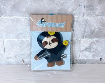 May include: A plush sloth toy in a black outfit, packaged in a clear plastic bag. The sloth has brown and tan fur with a smiling face. The packaging features the text "SAMRUAY" in blue and a sloth illustration.