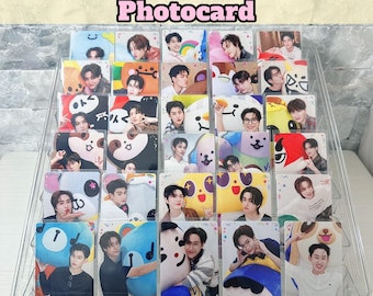 May include: A clear acrylic tiered display stand holding a collection of rectangular photocards featuring various individuals posing with colorful cartoon character illustrations. The text Happy Fam Bons Photocard and Ninimyle is visible.
