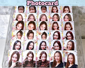 May include: A clear acrylic display case filled with photocard sets. Each card features a young woman making a heart shape with her hands. The text "Girls Selfie Heart Shot Photocard" is at the top, and "NINIMYLE" is at the bottom.