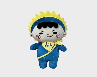 May include: A plush doll featuring a yellow sun-shaped headpiece, a blue outfit with a star pattern, and a yellow neck scarf with the letter m. The doll has a white face, black hair, and red spiral cheeks, with a GMMTV logo in the top corner.