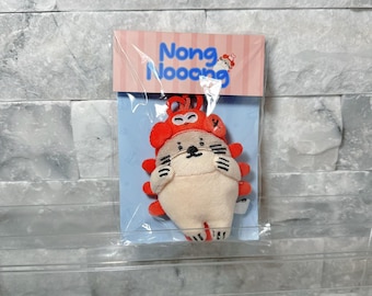 May include: A plush keychain featuring a cream-colored character wearing a bright orange lobster hat. The character has embroidered facial features and black whiskers. It is packaged on a light blue card with the text Nong Nooong at the top.