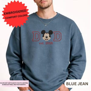 A man wearing a blue sweatshirt with a Mickey Mouse design and text printed on it.