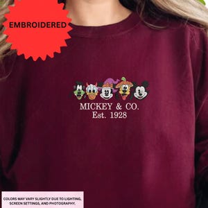 A close-up of a person wearing a burgundy shirt with a red starburst logo and a line of Mickey Mouse faces.