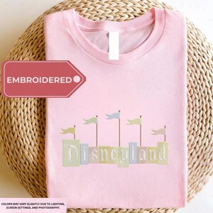 A pink t-shirt with the word "Disneyland" embroidered on it, along with a tag that says "EMBROIDED".