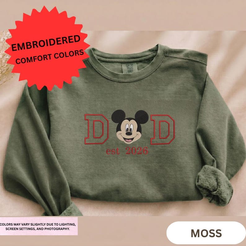 a green long-sleeved shirt with a red and black design on it, including a Mickey Mouse logo and the text "D.D. est 2026".