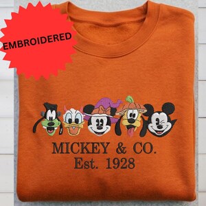 a bright orange t-shirt with a large embroidered design of the Disney characters Mickey Mouse and Co.