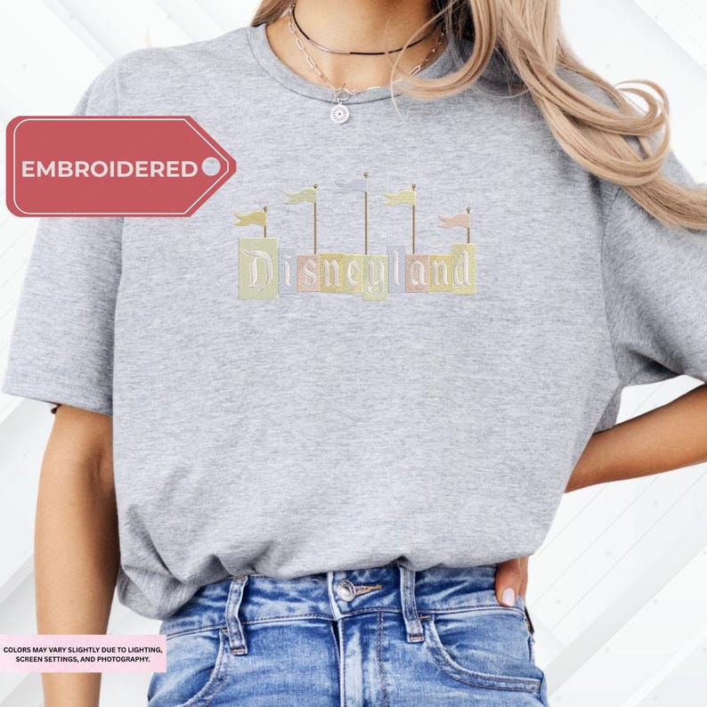 A woman wearing a gray t-shirt with the word "Disneyland" embroidered on it, paired with blue jeans.