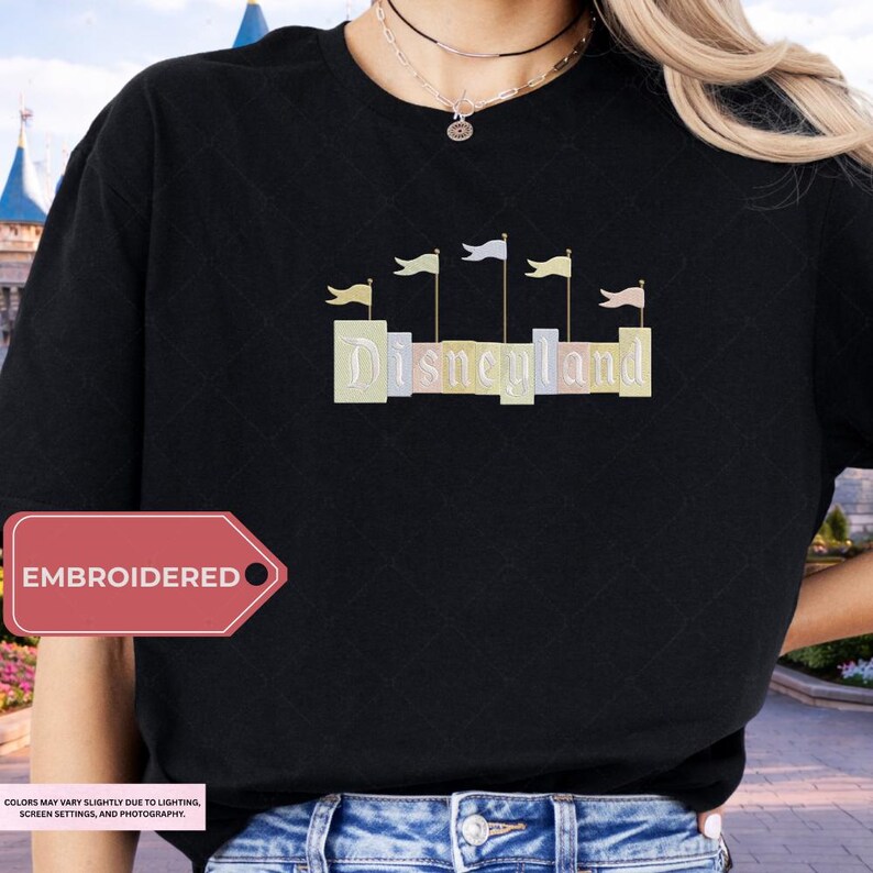 A person wearing a black t-shirt with the word "Disneyland" embroidered on it, standing in front of a Disney castle.